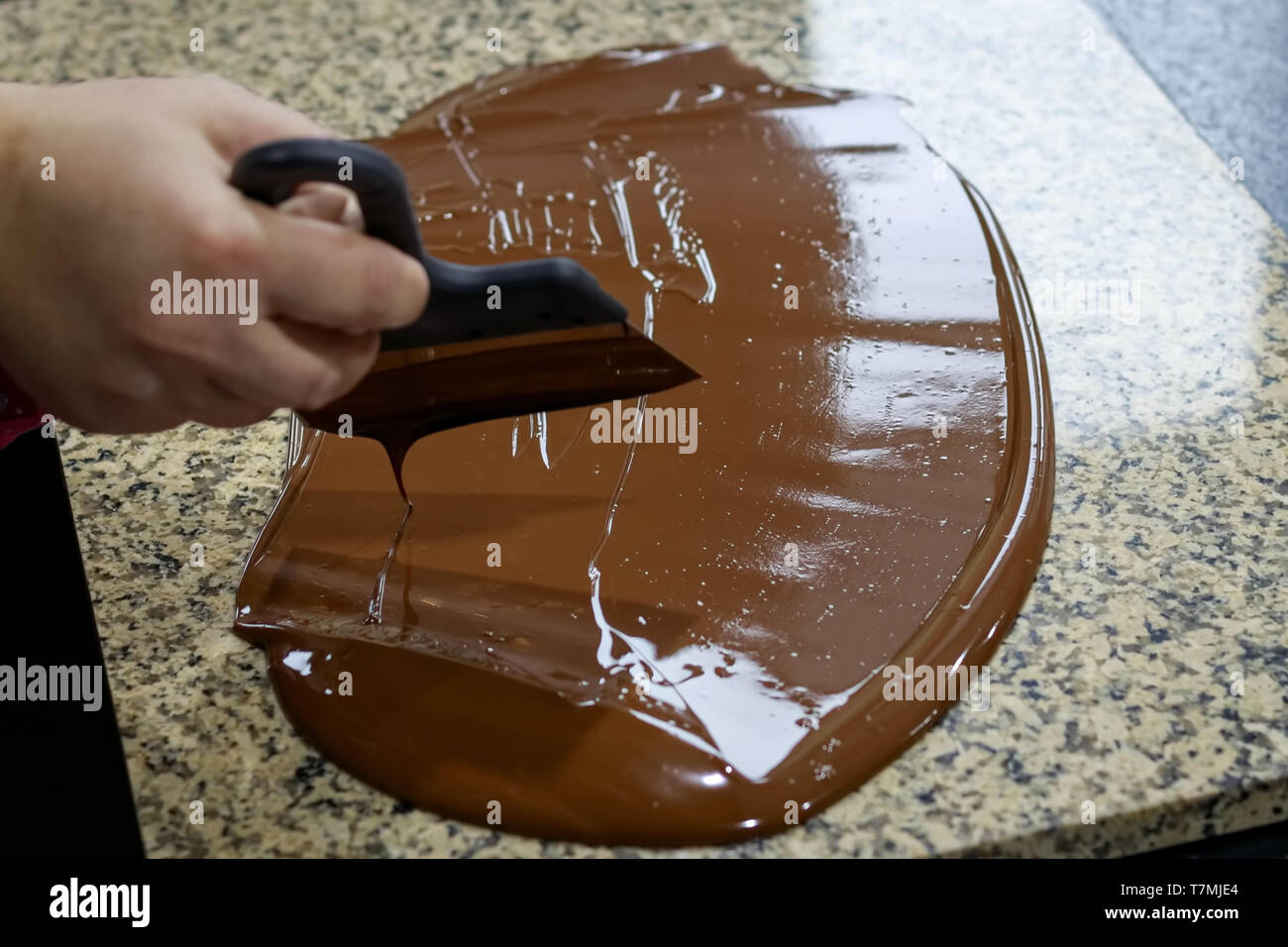 Chocolatier rührt die temperierte Schokolade auf einem Klapptisch, die zur Kühlung Stockfoto