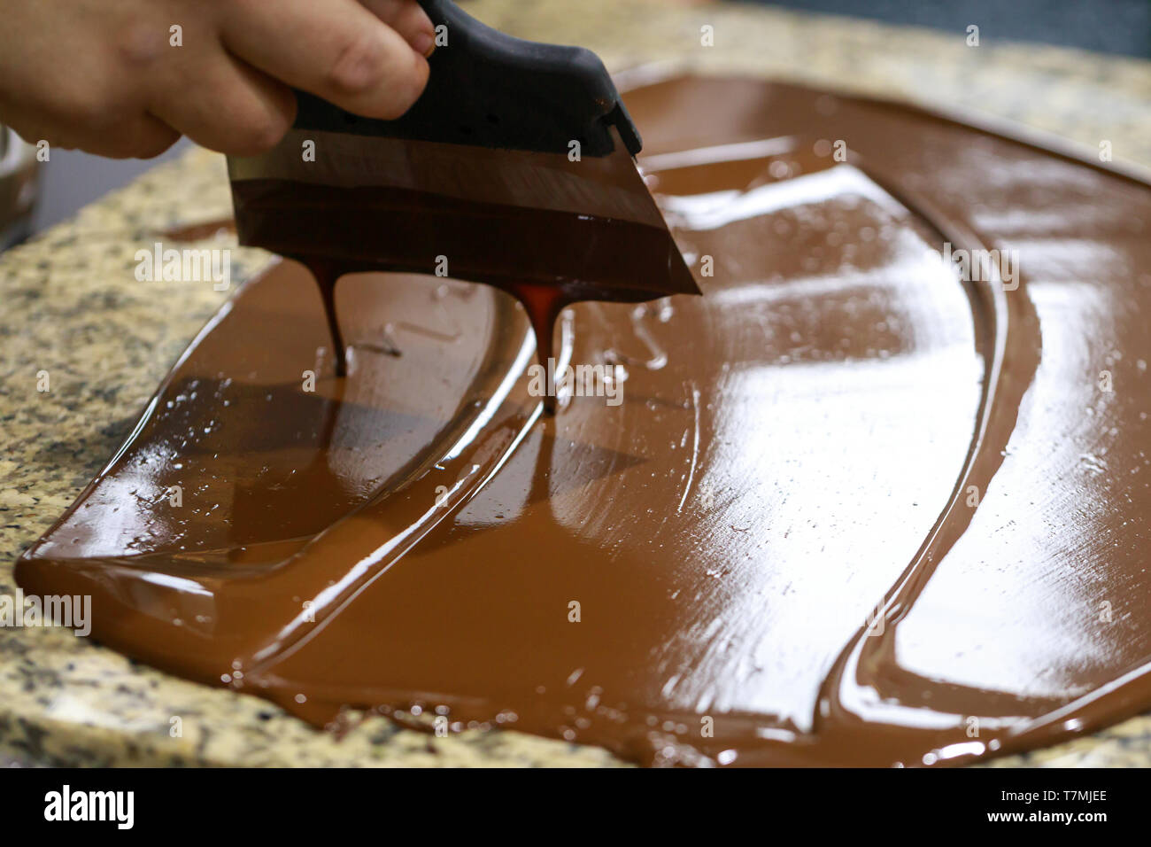 Chocolatier mit einem Teigschaber, rührt die temperierte flüssige Schokolade auf einem Granit Tisch Stockfoto