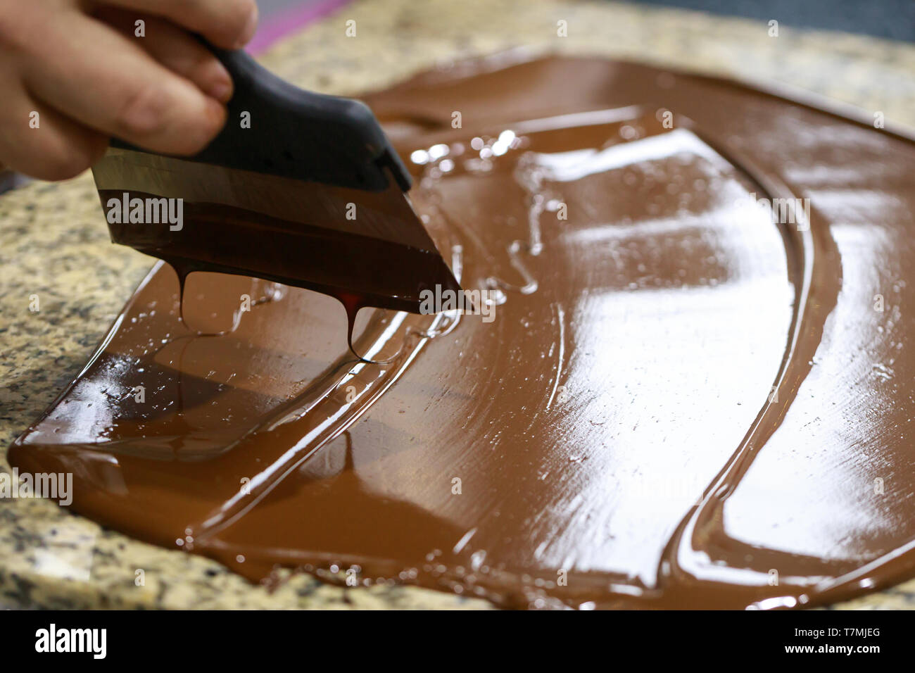 Chocolatier mit einem Teigschaber, rührt die temperierte flüssige Schokolade auf einem Granit Tisch Stockfoto