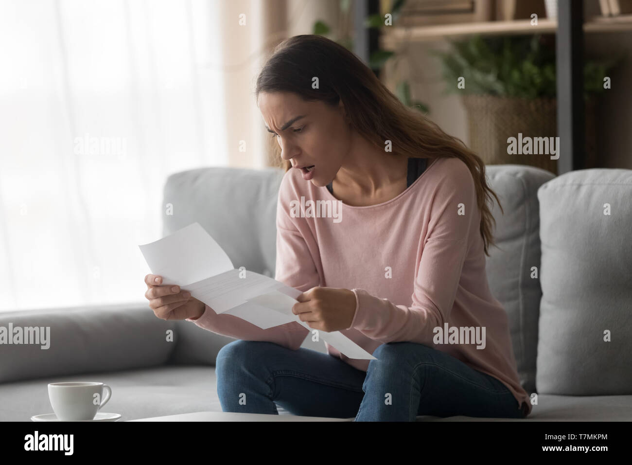 Wütende Frau sitzt auf der Couch halten Schreiben schlechte Nachrichten Stockfoto