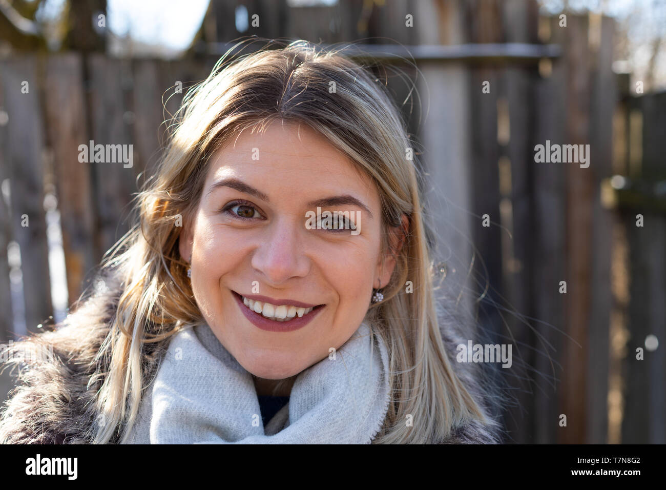 Porträt einer schönen jungen Frau mit warmen Mantel und grauen Schal, lächelnd in die Kamera vor der Weinlese Zaun Stockfoto