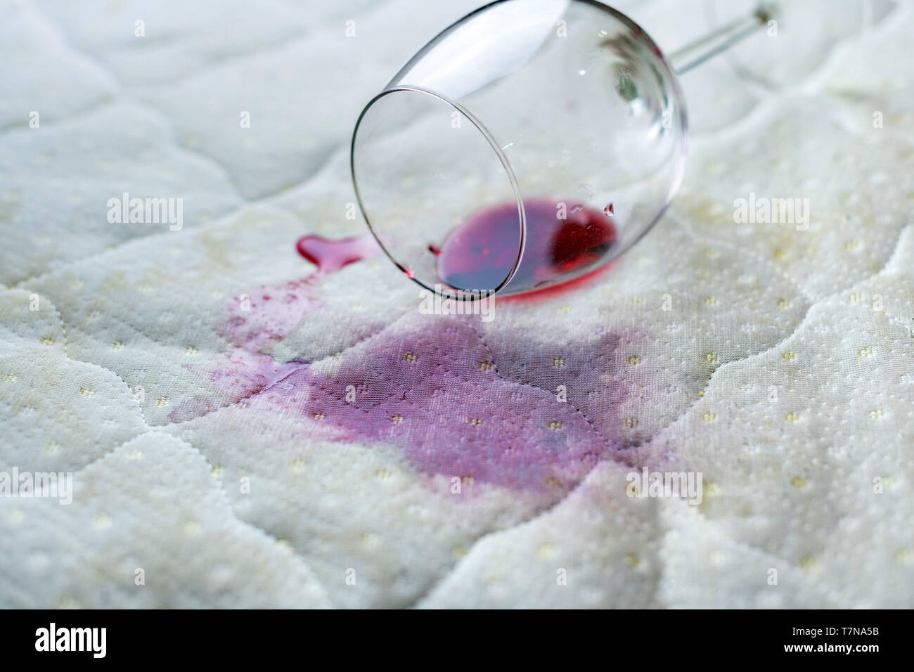 Wein Glas verschüttet auf dem Bett. Fallengelassen Weinglas auf weißen Bettlaken. Rosa nassen Fleck. Pech, unglückliche Situation. Stockfoto