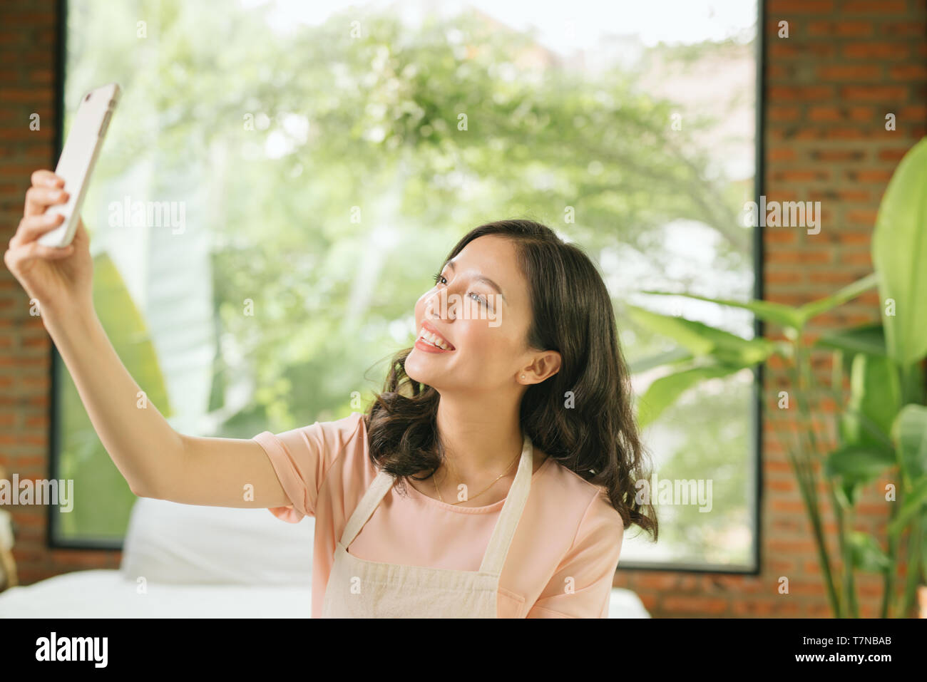 Schöne junge Frau hält ein Mop, mit einem Smartphone und lächelnd, während Ihr Haus Reinigung Stockfoto