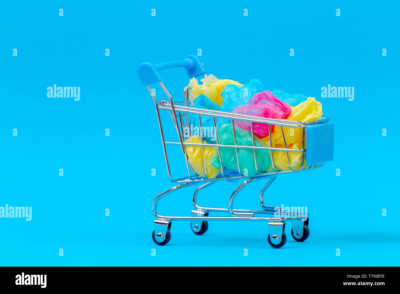 Mini Einkaufswagen voller bunter single use Plastiktüten auf blauem Hintergrund Stockfoto