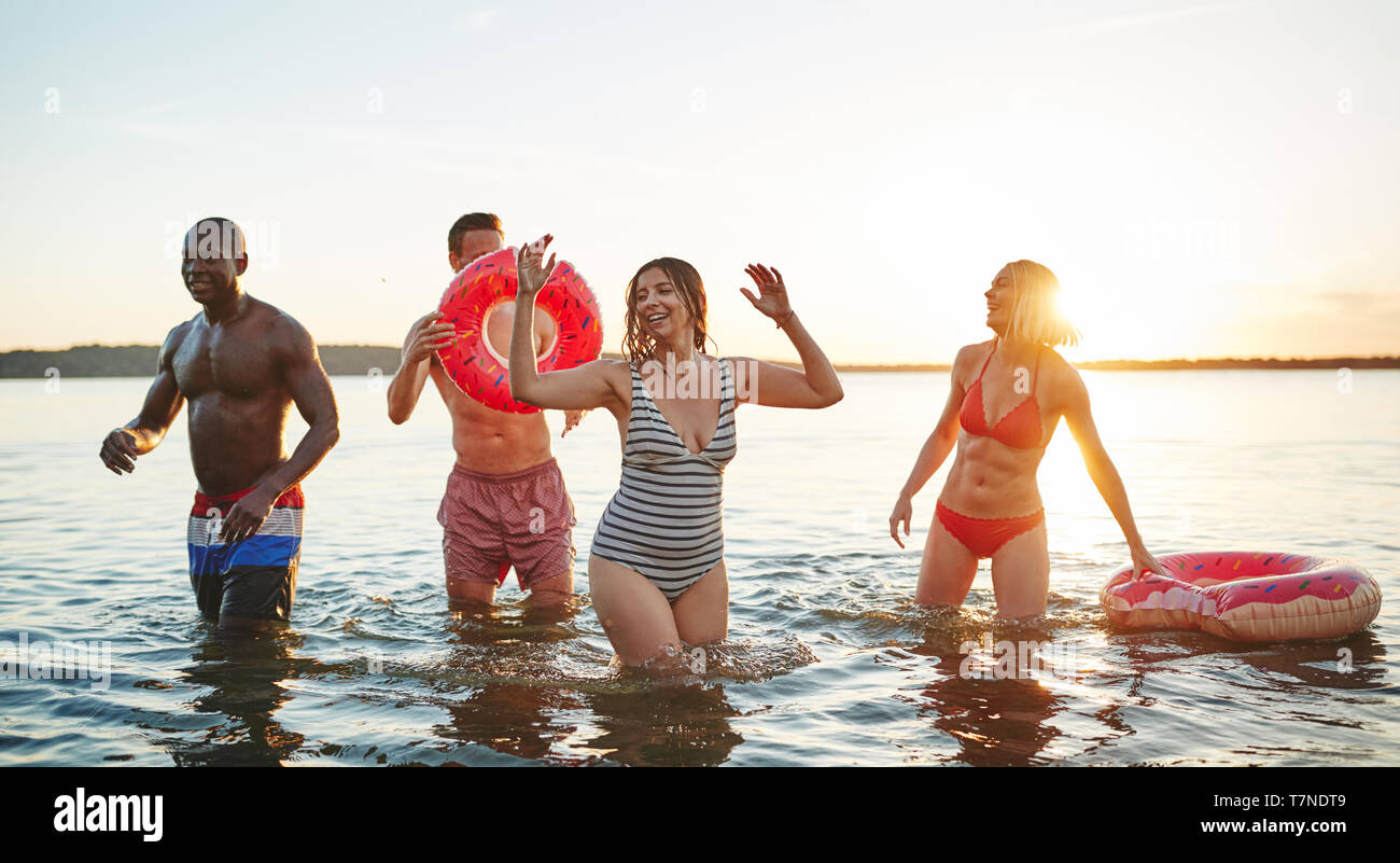 Vielfältige Gruppe von jungen Freunde lachen und Spritzwasser an einander in einem See auf einer späten Sommer afternon Stockfoto