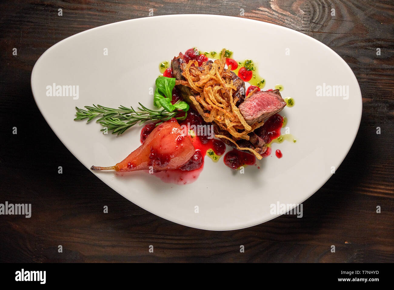 Fleisch Steak mit Birne auf einem weißen Teller mit grünen: Rosmarin, Basilikum und Spinat eingerichtet. Dunklen Hintergrund. Das Essen im Restaurant. Stockfoto