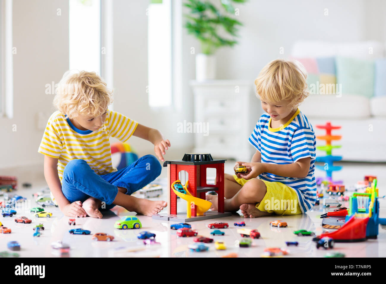 Kinder spielen mit Spielzeug Autos in weißen Raum. Kleiner Junge beim Spielen mit Auto- und LKW-Spielzeug. Fahrzeug und Verkehr Spiel für Kinder. Kind mit Parkplatz Gara Stockfoto