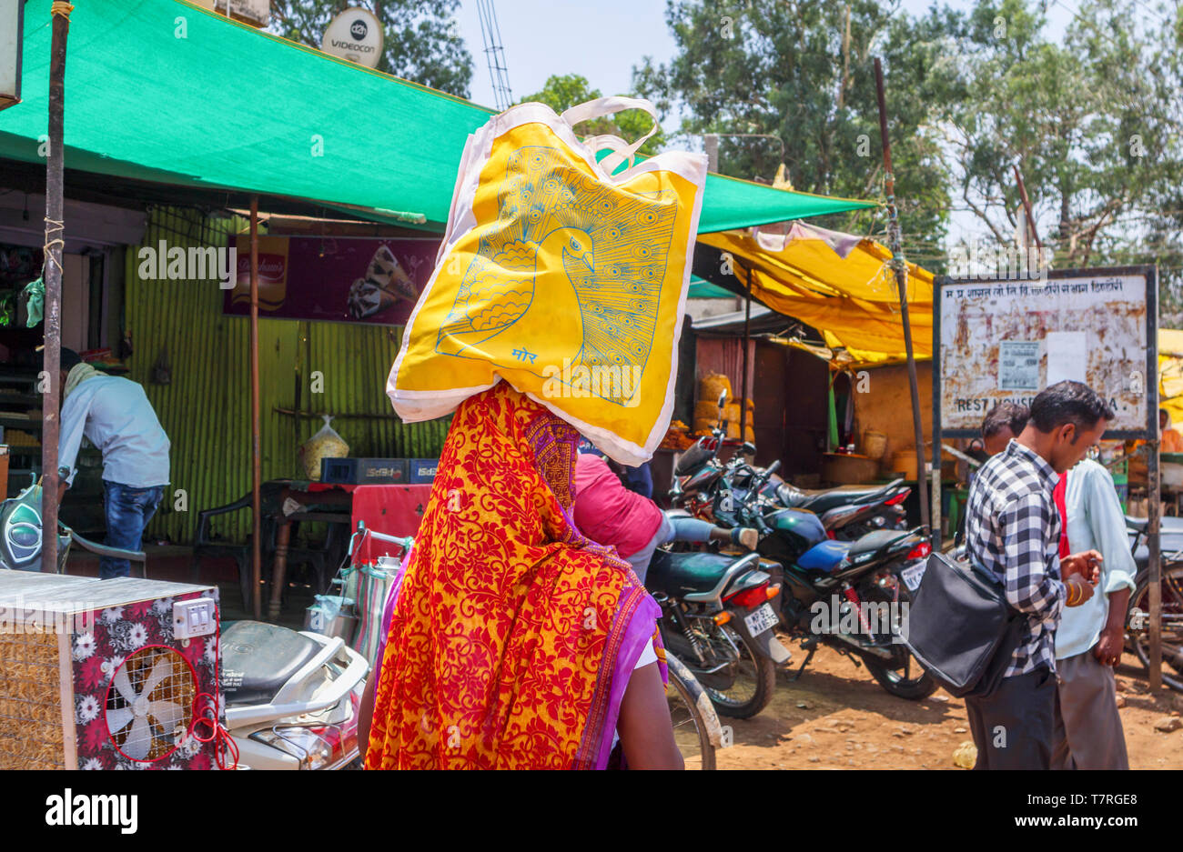 Straßenszene in Shahpura, ein dindori Kreisstadt in Madhya Pradesh, Indien: Eine lokale Frau mit einer Einkaufstasche auf dem Kopf Stockfoto