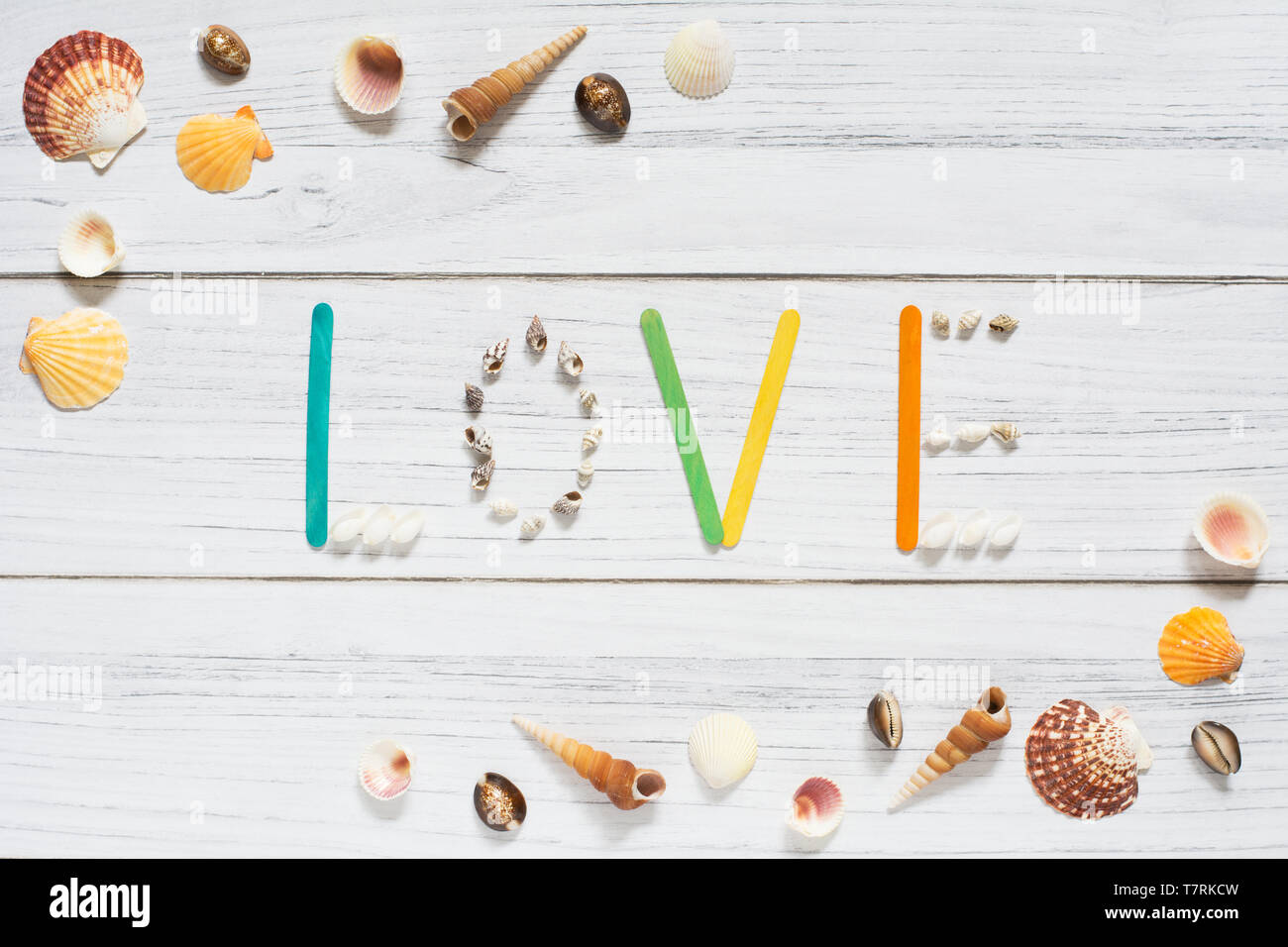 Sommer Grenze mit Muscheln und 'Liebe' Zeichen in der Mitte auf weißem Holz- Hintergrund Stockfoto