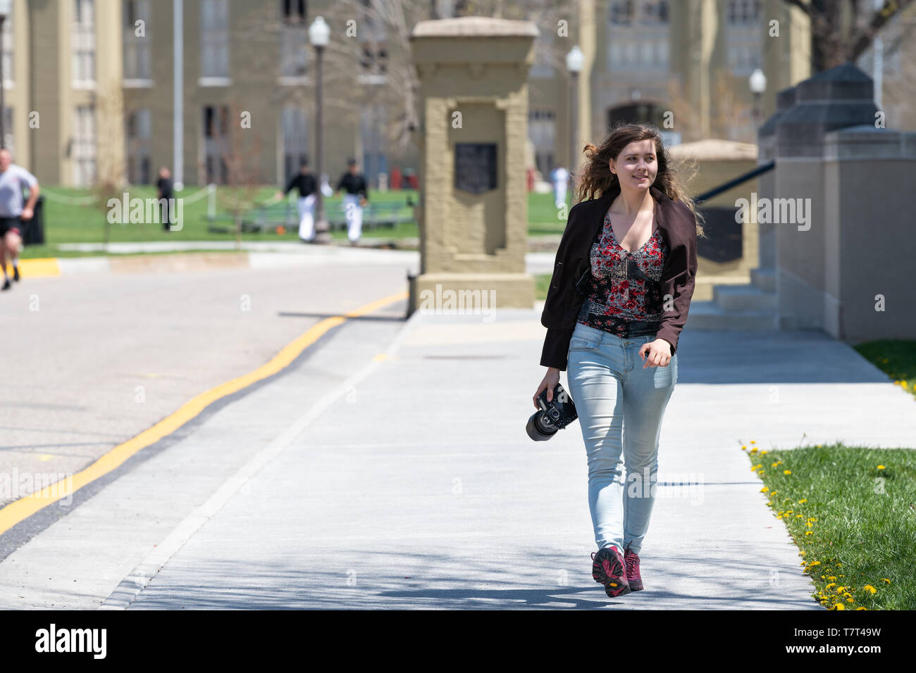 Lexington, USA - 18. April 2018: junge lächelnde Frau, professioneller Fotograf mit DSLR-Kamera zu Fuß auf dem Bürgersteig auf dem Campus der Virginia Mil Stockfoto