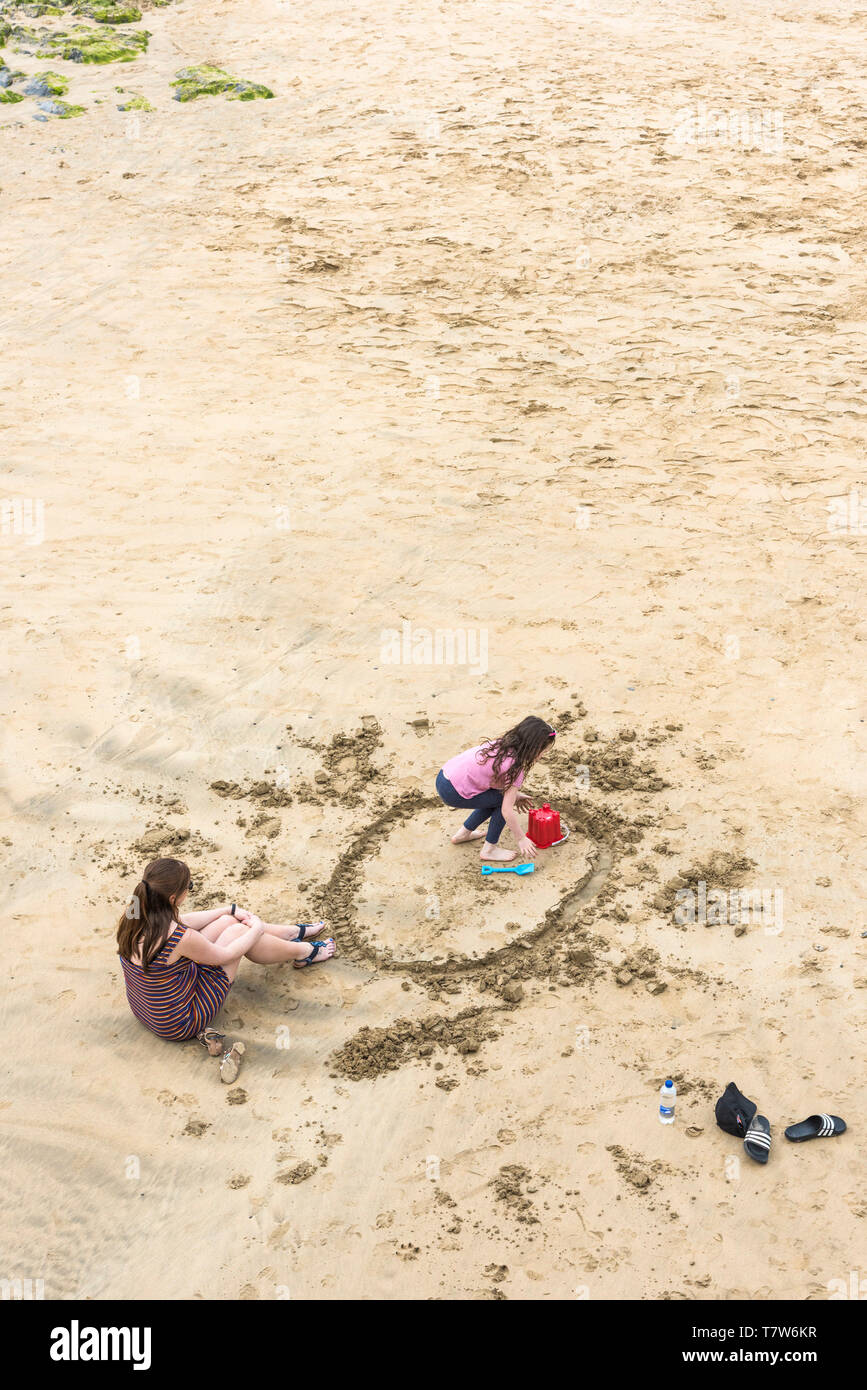 Eine Mutter beobachten ihre junge Tochter beim Spielen im Sand auf den Towan Strand in Newquay in Cornwall. Stockfoto