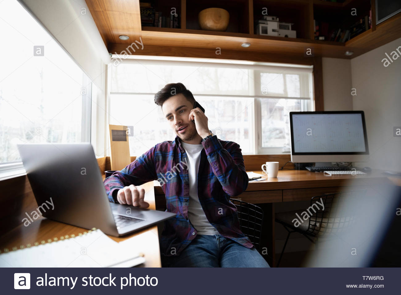 Junger Mann zu Hause arbeiten, Telefonieren Handy mit Laptop im Home Office Stockfoto