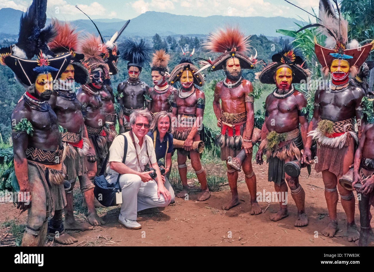 Zwei Amerikaner posieren für ein Foto mit den Huli Wigmen das Paar während einer traditionellen Singen fotografiert hatte - singen Zeremonie an Tari im Südlichen Hochland von Papua Neuguinea (PNG), eine Fernbedienung und robuste Land im Pazifischen Ozean vor der nordöstlichen Spitze von Australien. Vor schlagen Ihre kleinen Trommeln und Tanzen im Einklang, diese männlichen Krieger verbringen Stunden selbst dekorieren durch Lackieren von Flächen und Körpern und tragen Hut - wie Perücken mit bunten Federn geschmückt. Singen - singt in der Vergangenheit wurden oft Präludien Kriegsführung zu Tribal aber heutzutage bieten Unterhaltung für Einheimische und Touristen. Stockfoto