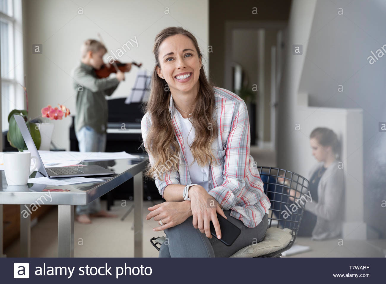 Portrait zuversichtlich, glückliche Mutter von zu Hause aus zu arbeiten, während die Kinder die Hausaufgaben und Praxis Violine im Hintergrund tun Stockfoto