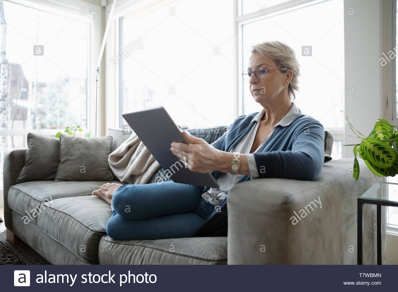 Reife Frau mit digitalen Tablette auf Sofa im Wohnzimmer Stockfoto