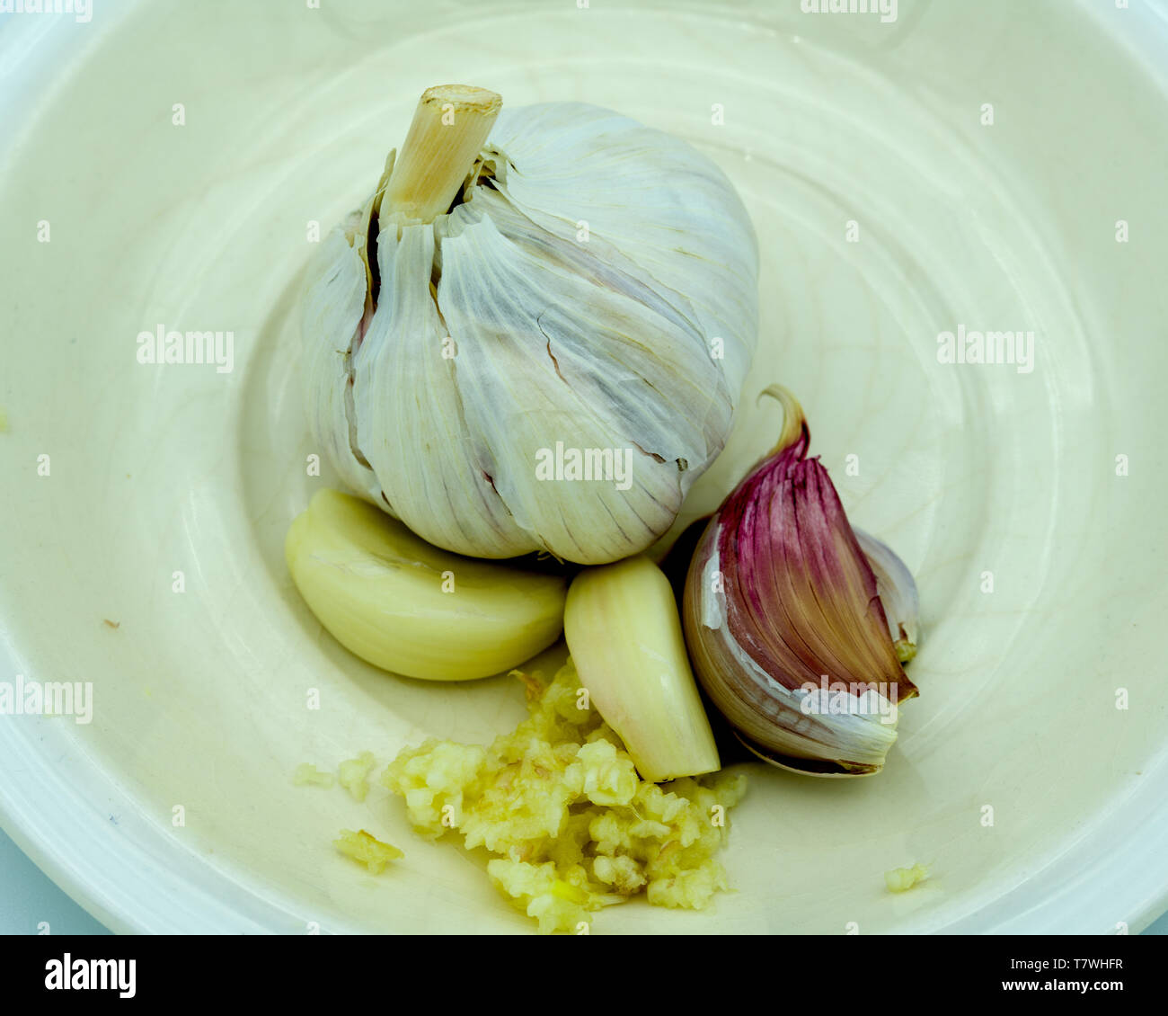 Frische Knoblauchzwiebeln, Zehen und gehackter Knoblauch zusammen auf einer weißen Untertasse. Stockfoto