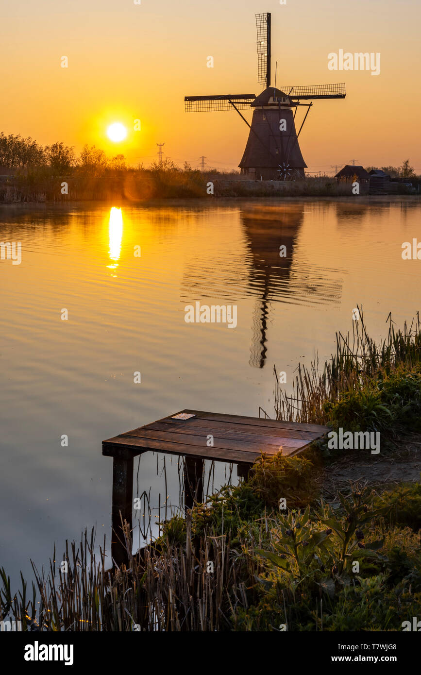 Embarquement am Rand mit dem ruhigen Wasser des langen Kanals während mit Blick auf eine Windmühle Reflexion in der Brennen sunrise Farbe morgen Stockfoto