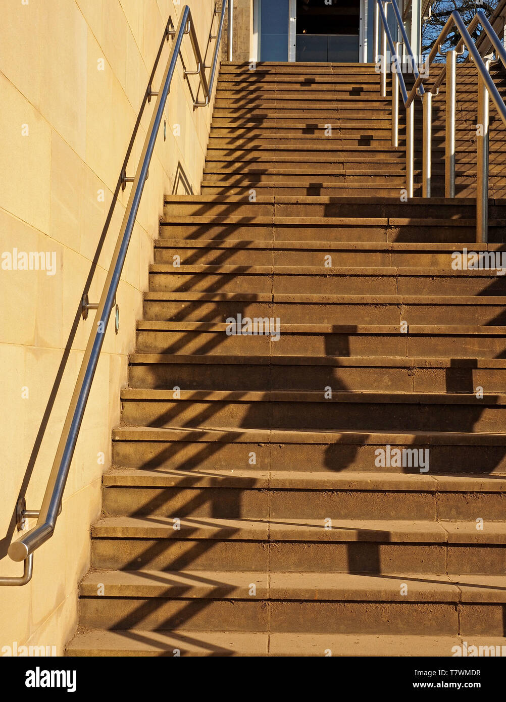 Faltlagen und Linien - Muster der Schatten von parallelen Stahl Geländer auf lange Steintreppe im hellen Sonnenschein in West Yorkshire, England, Großbritannien Stockfoto