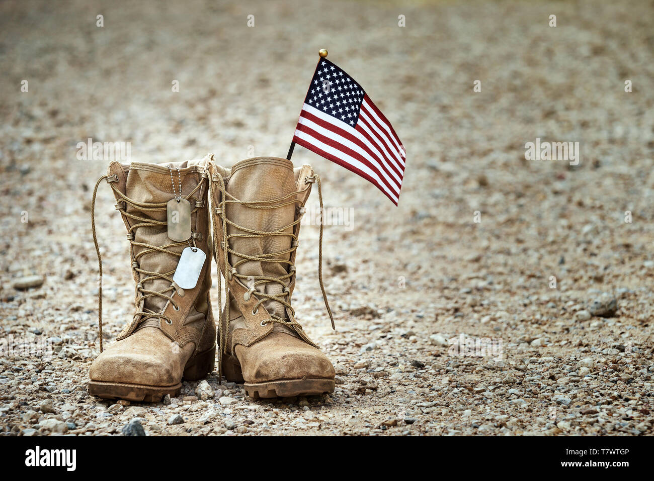 Alte militärische Bekämpfung Stiefel mit Dog Tags und eine kleine amerikanische Flagge. Felsigen Kies Hintergrund mit kopieren. Memorial Day, Tag Veteranen, Opfer conc Stockfoto