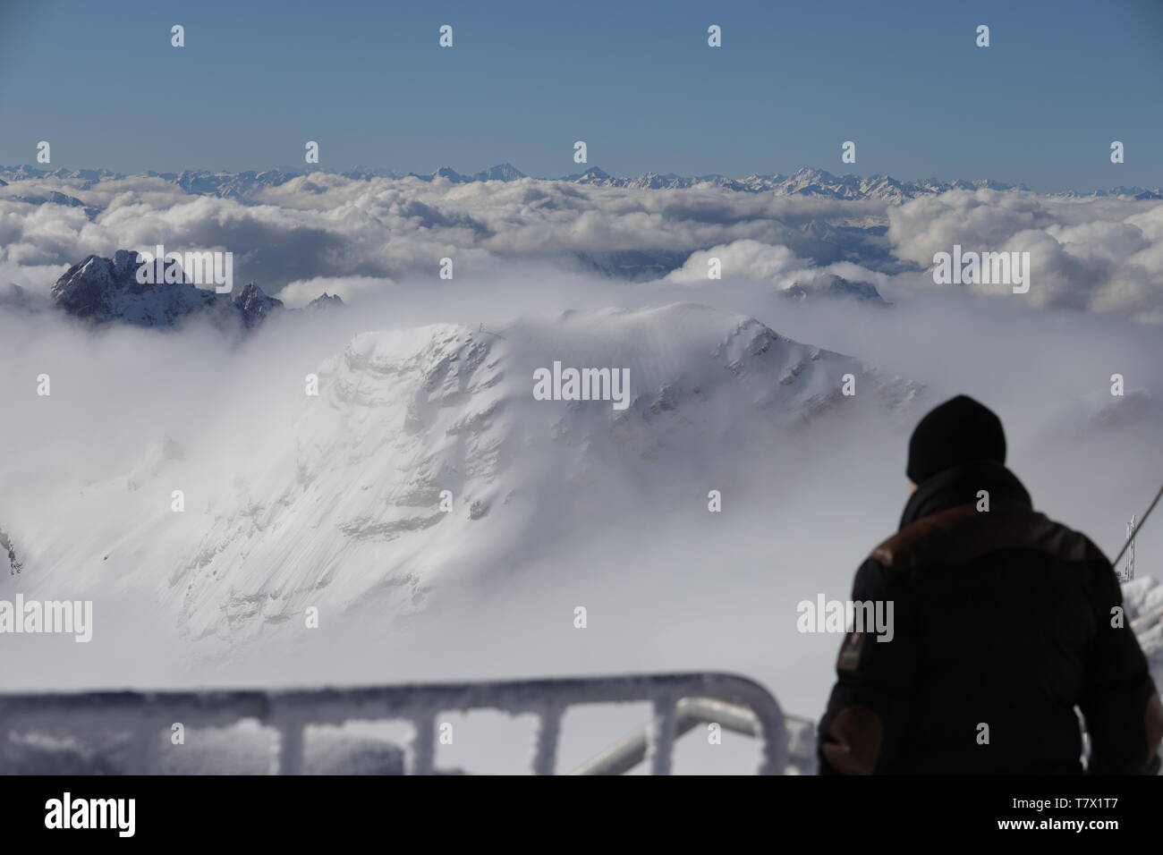 Zugspitze: Ein Besucher betrachtet von der Aussichtsplattform das überfältigte Zusammenspiel von Schnee, Wolken, blauem Himmel und Sonne. Stockfoto