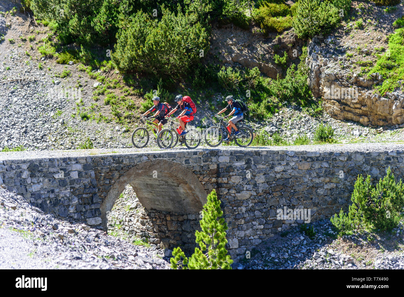 Drei junge Mountainbiker über eine alte Steinbrücke in den Alpen Stockfoto