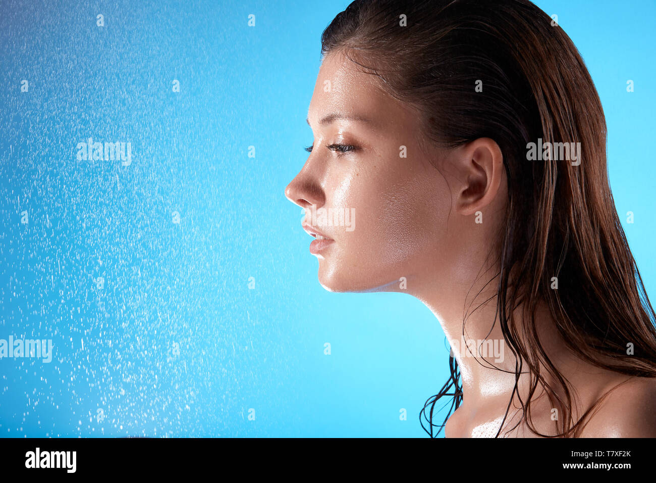 Frische Frau mit nassem Haar und Gesicht auf blauem Hintergrund mit Spritzwasser, Kopieren, schöne Mädchen nach der Dusche Stockfoto