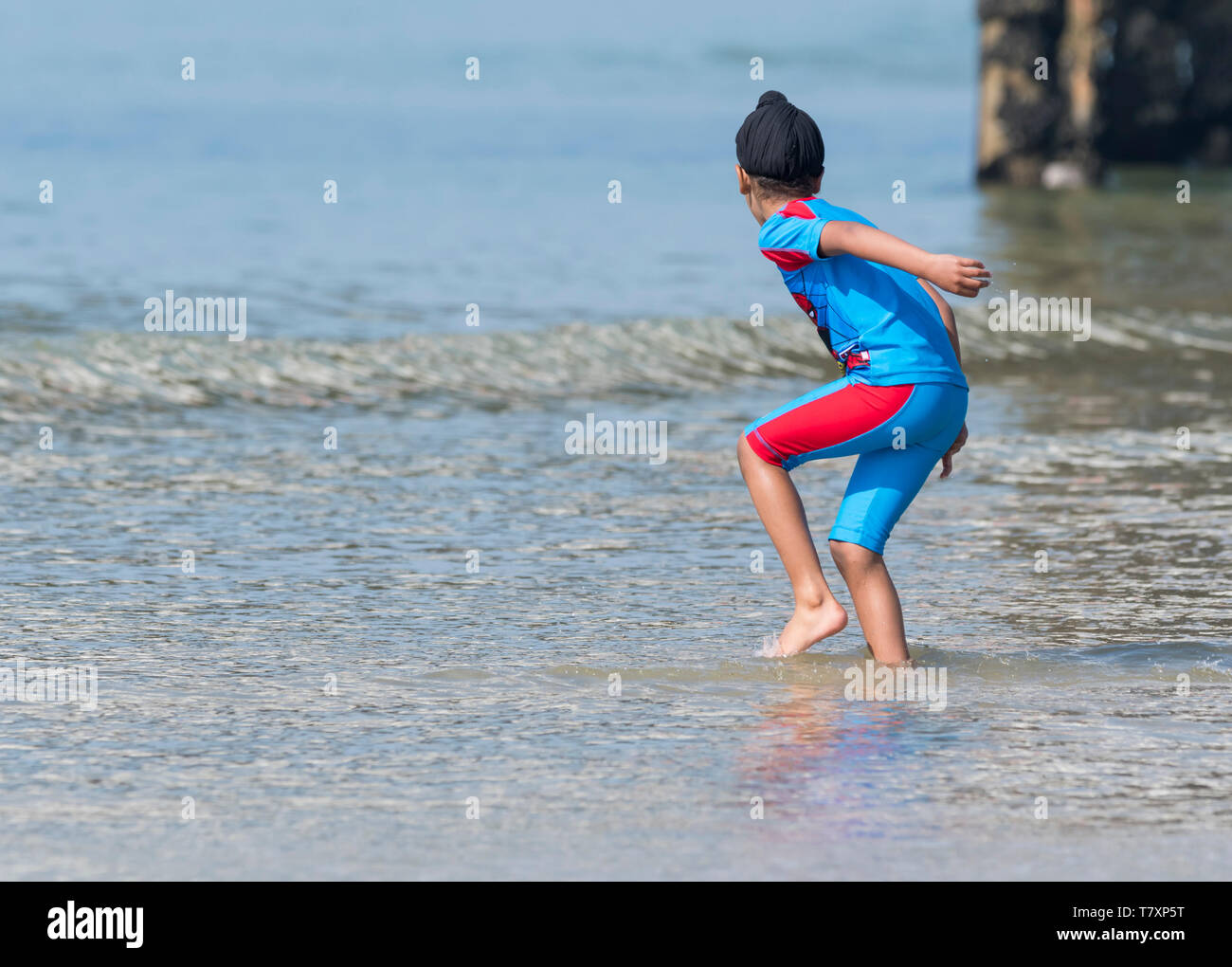 Junge trägt einen Turban Paddeln im Meer im Frühling in Brighton, East Sussex, England, UK. Kind mit Turban. Vermutlich ein Sikh. Stockfoto