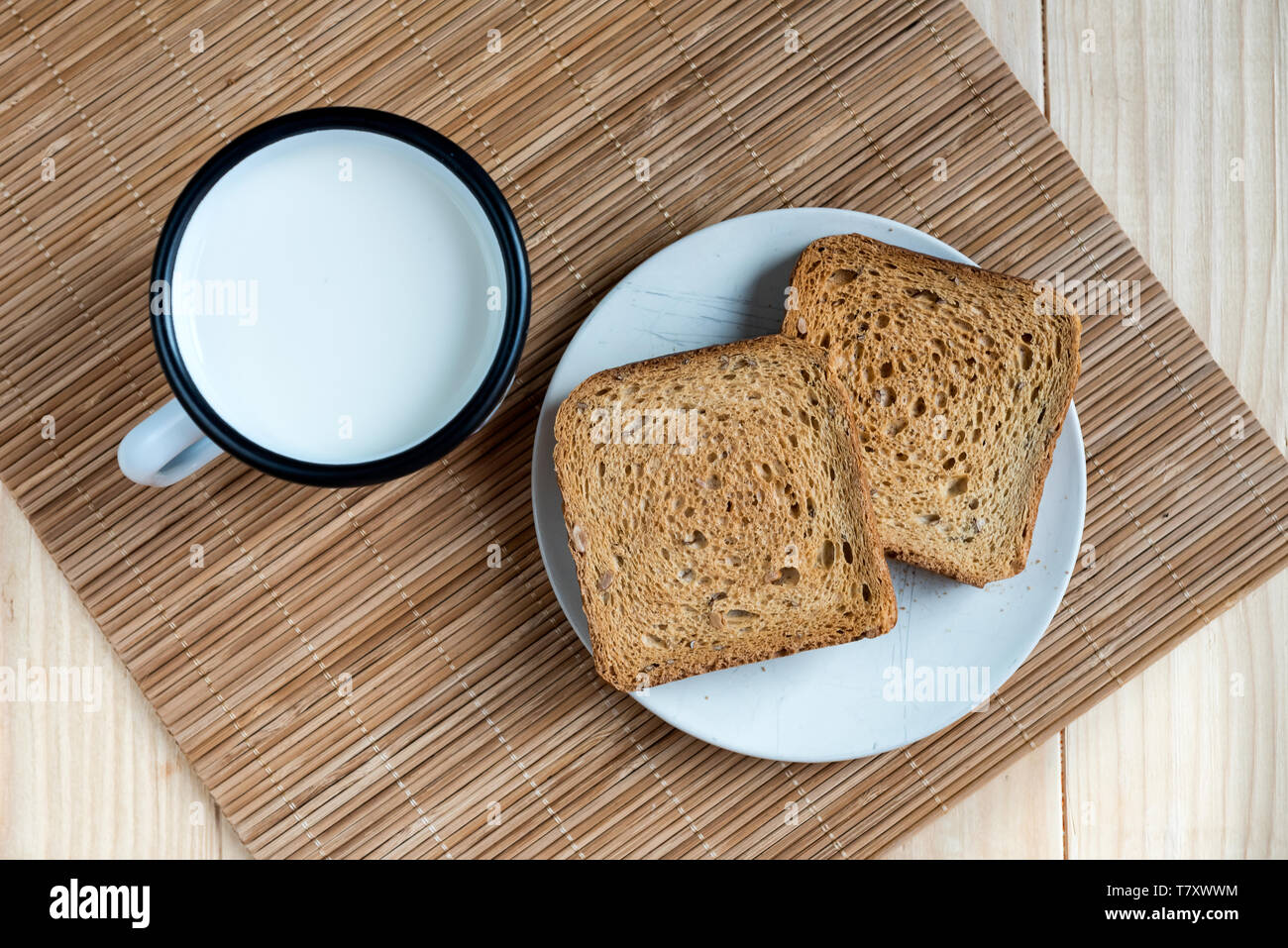 Zwei Scheiben Toast Brot und Zinn Becher Milch auf einem Holztisch, Setup Stockfoto