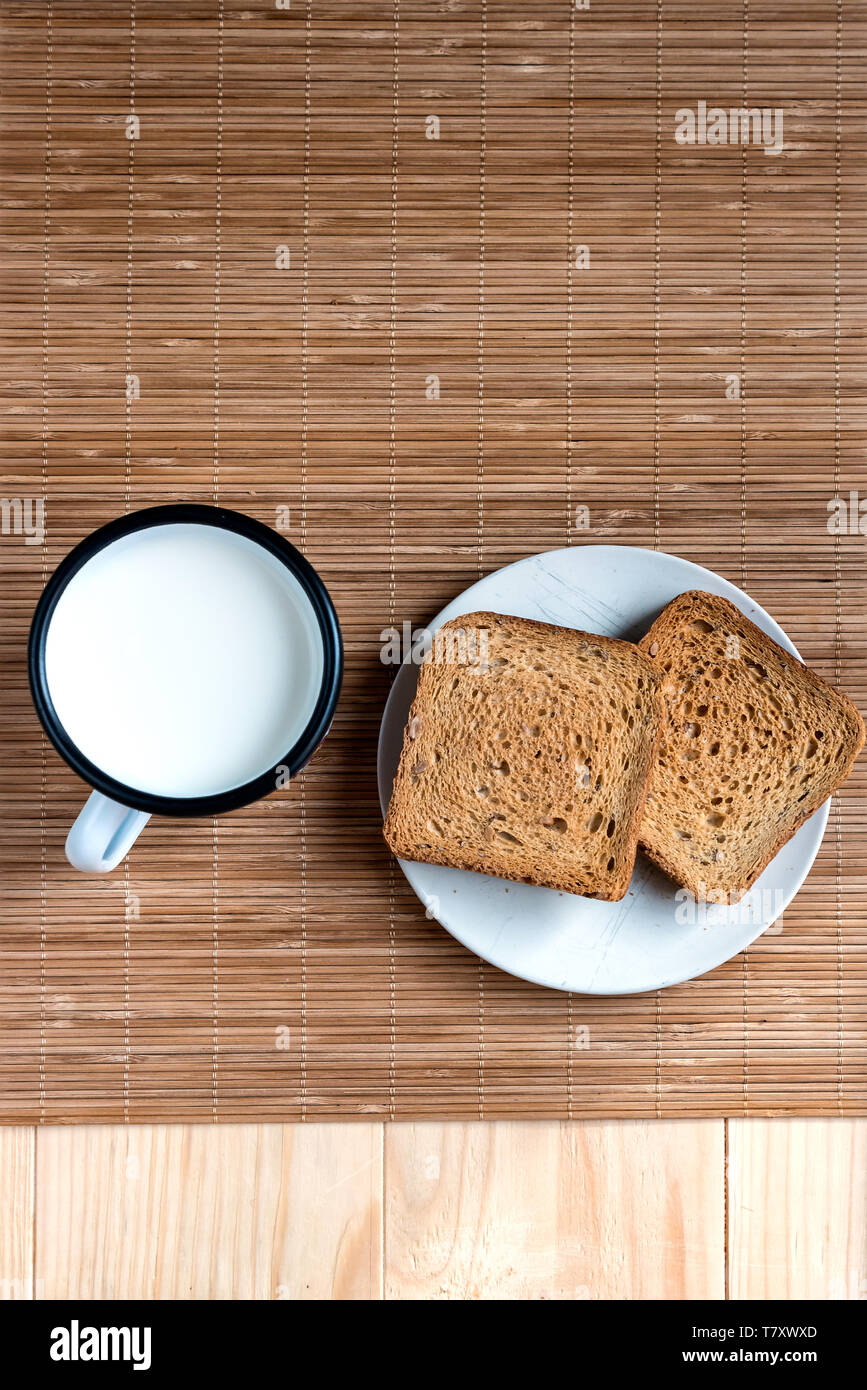 Zwei Scheiben Toast Brot und Zinn Becher Milch auf einem Holztisch, Setup Stockfoto