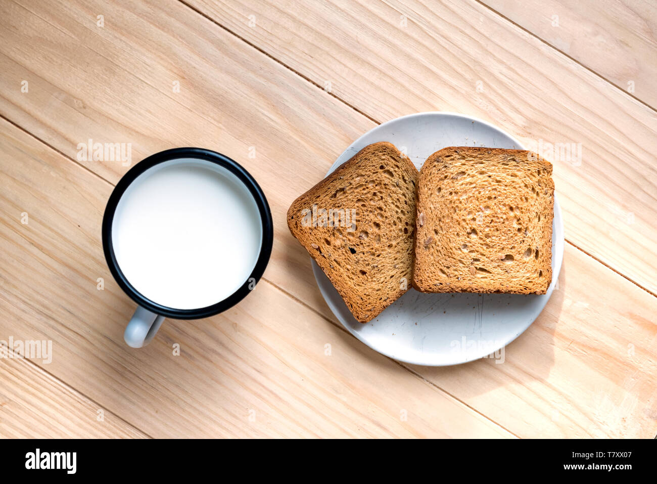 Zwei Scheiben Toast Brot und Zinn Becher Milch auf einem Holztisch, Setup Stockfoto