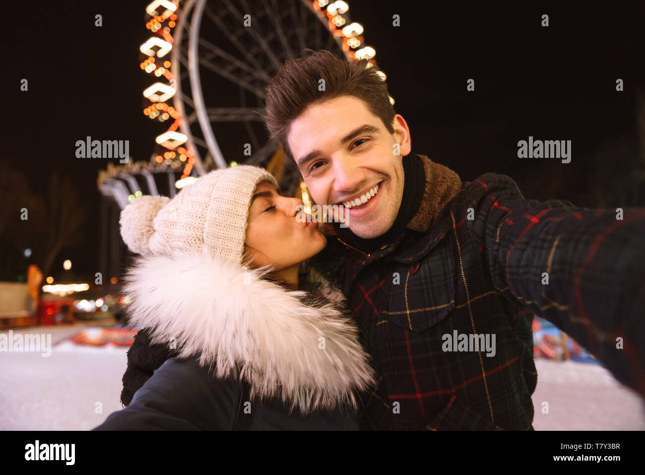 Gerne fröhliche junges Paar, das Spaß am Eislaufen Park bei Nacht, wobei ein selfie, küssen Stockfoto