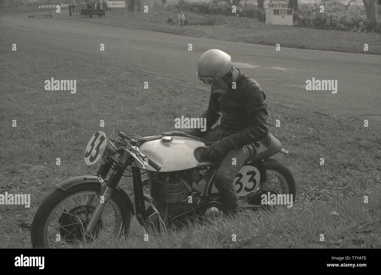1960, historische, eine niedergeschlagen, enttäuscht racing Motorradfahrer auf dem Gras neben der Schiene im Oulton Park Rennstrecke, das gehabt hat aus dem Rennen, England, Großbritannien, in den Ruhestand geparkt. Stockfoto