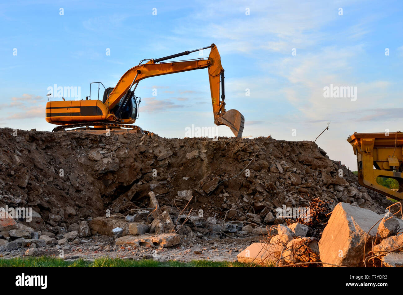 Schwere bagger Schaufel im Steinbruch arbeiten auf einem Hintergrund von Sonnenuntergang und blauer Himmel. Mobile kiefer Steinbrecher von der Baustelle. Crushing alte concr Stockfoto