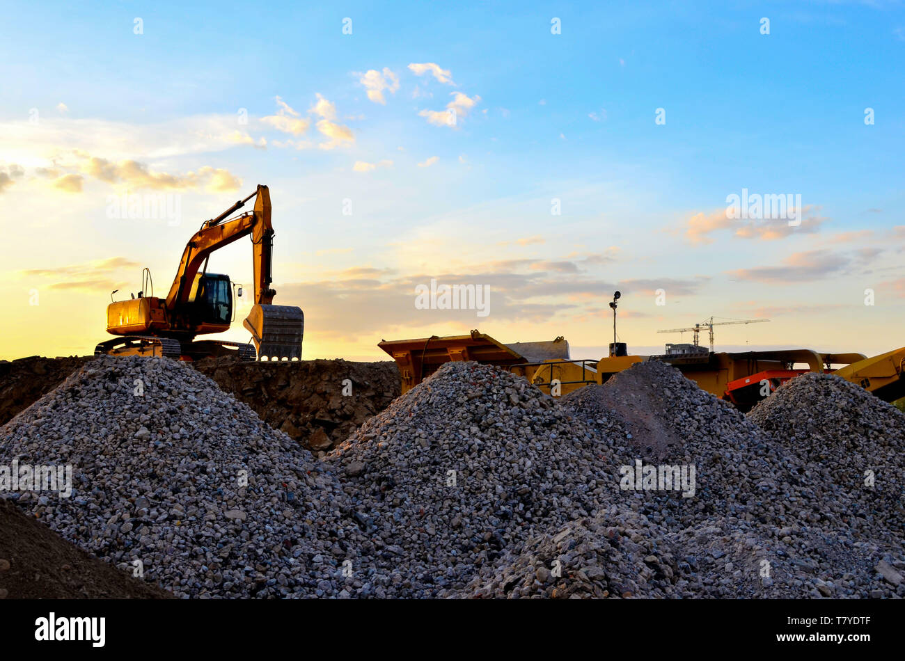 Schwere bagger Schaufel im Steinbruch arbeiten auf einem Hintergrund von Sonnenuntergang und blauer Himmel. Mobile kiefer Steinbrecher von der Baustelle. Crushing alte concr Stockfoto