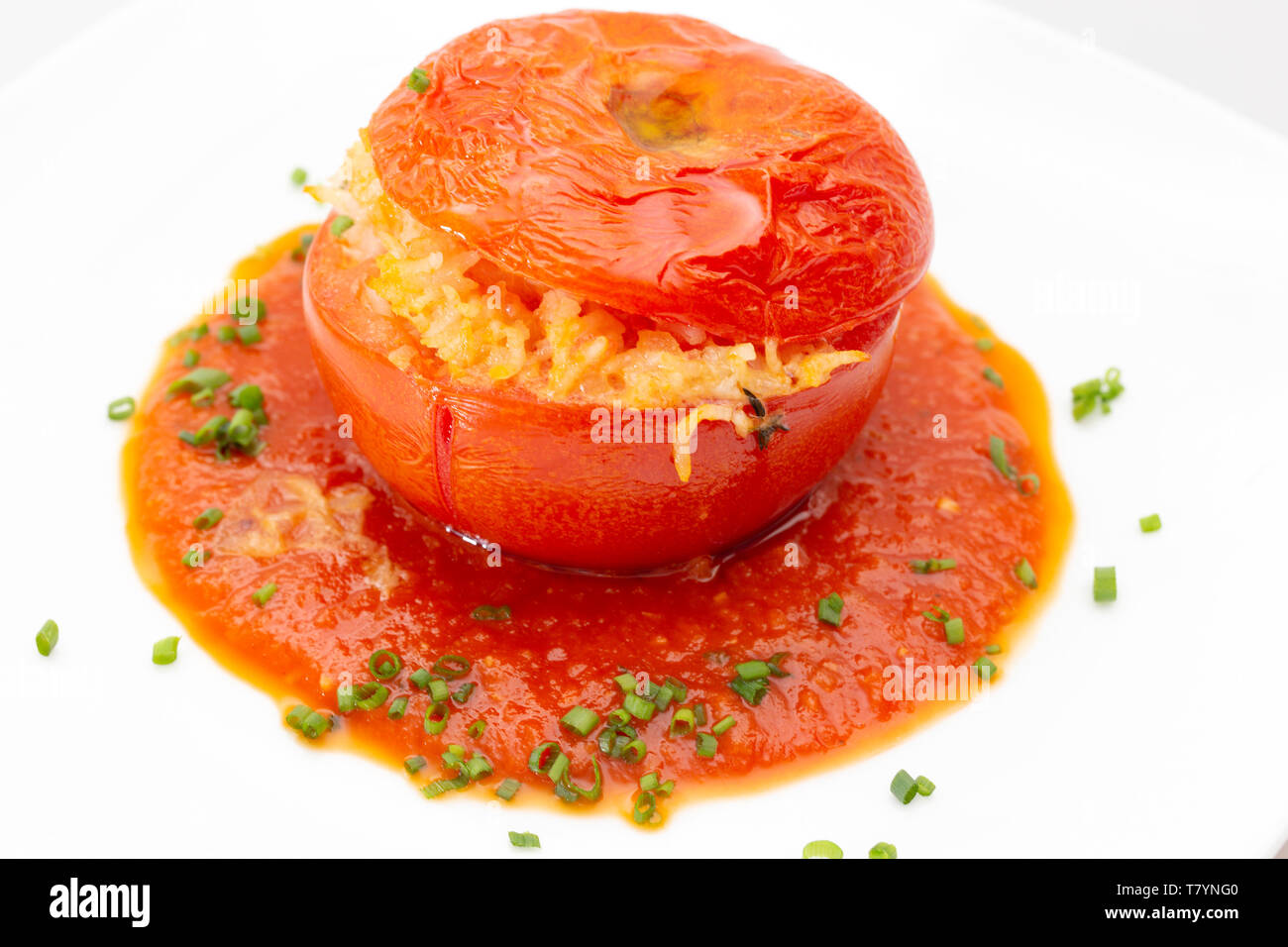 Eine Tomate gefüllt mit Reis und Gemüse, serviert auf einem Bett von Soße mit einer gehackten Schnittlauch garnieren. Stockfoto