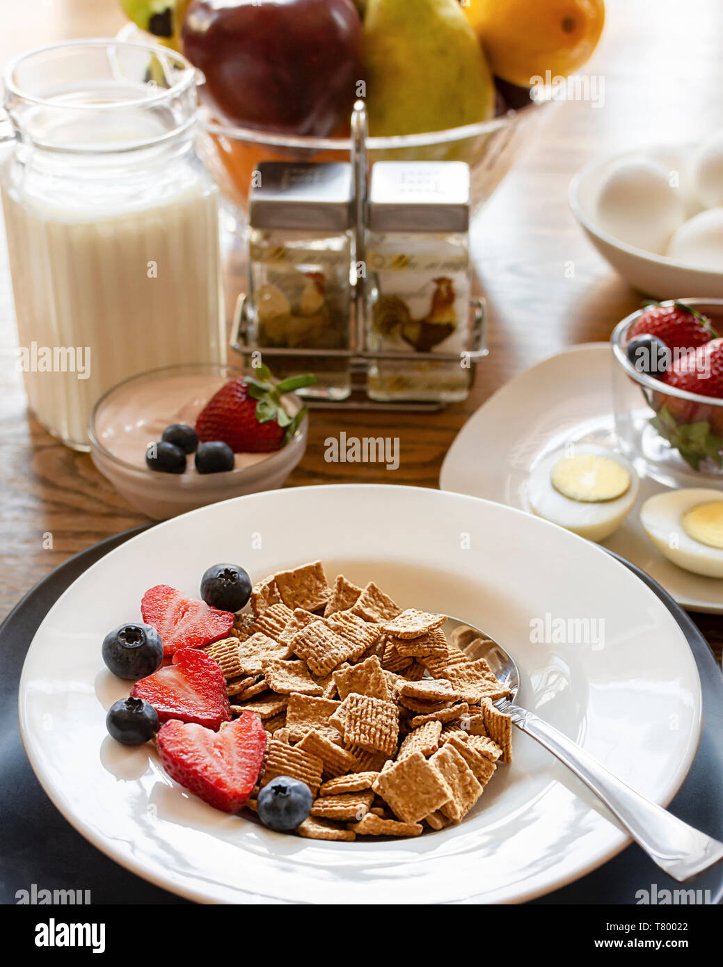 Eine Schüssel Müsli mit in Scheiben geschnittenen Erdbeeren und Blaubeeren als Teil einer ausgewogenen Frühstück. Eier, Obst, Joghurt und Milch blurre Stockfoto