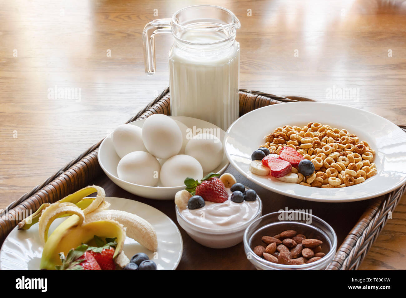 Eine Schüssel Hafer Getreide auf eine hölzerne Schale mit Joghurt, hart gekochte Eier, Bananen, Erdbeeren, Blaubeeren, Milch und Mandeln. Stockfoto