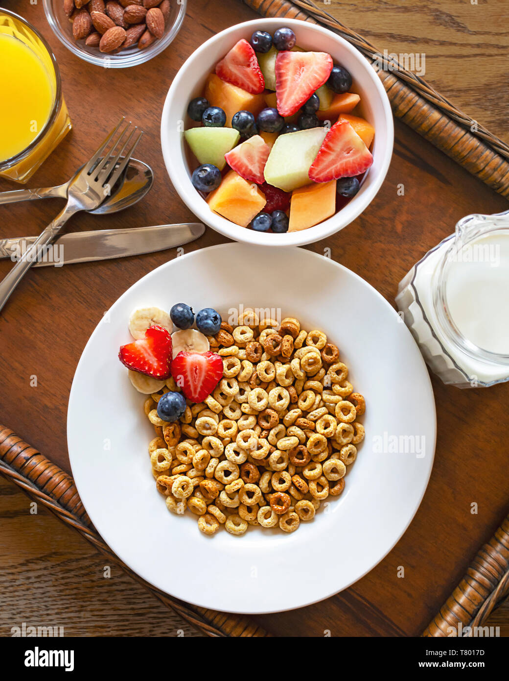 Flach aus einer Schüssel Hafer Müsli mit Früchten, Nüssen, Orangensaft und Milch auf Holz- Fach Fach ist auf einem hölzernen Tisch. Besteck enthalten. Stockfoto