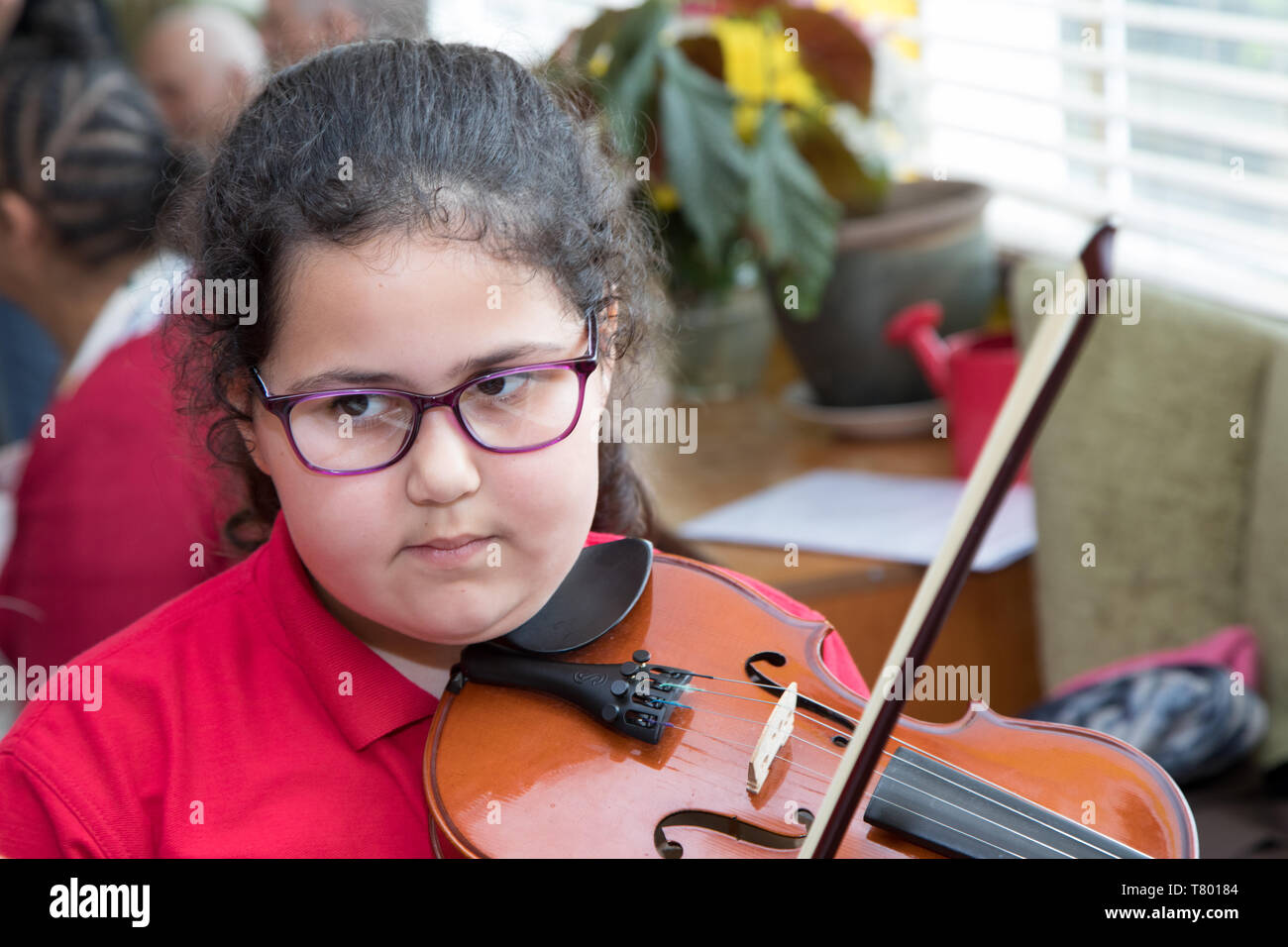 Eine Schule Mädchen spielt Geige. Sie ist zu Besuch in ein Pflegeheim für ältere Menschen mit ihrer Schule Stockfoto
