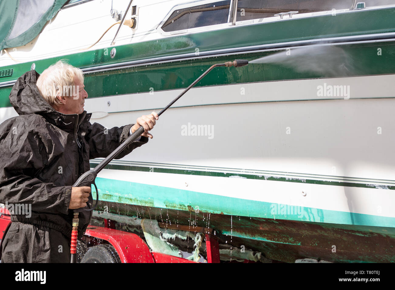 Kaukasische Mann mit schwarzen wasserdichten Anzug, während power Waschen schmutziger Bootsrumpf Stockfoto