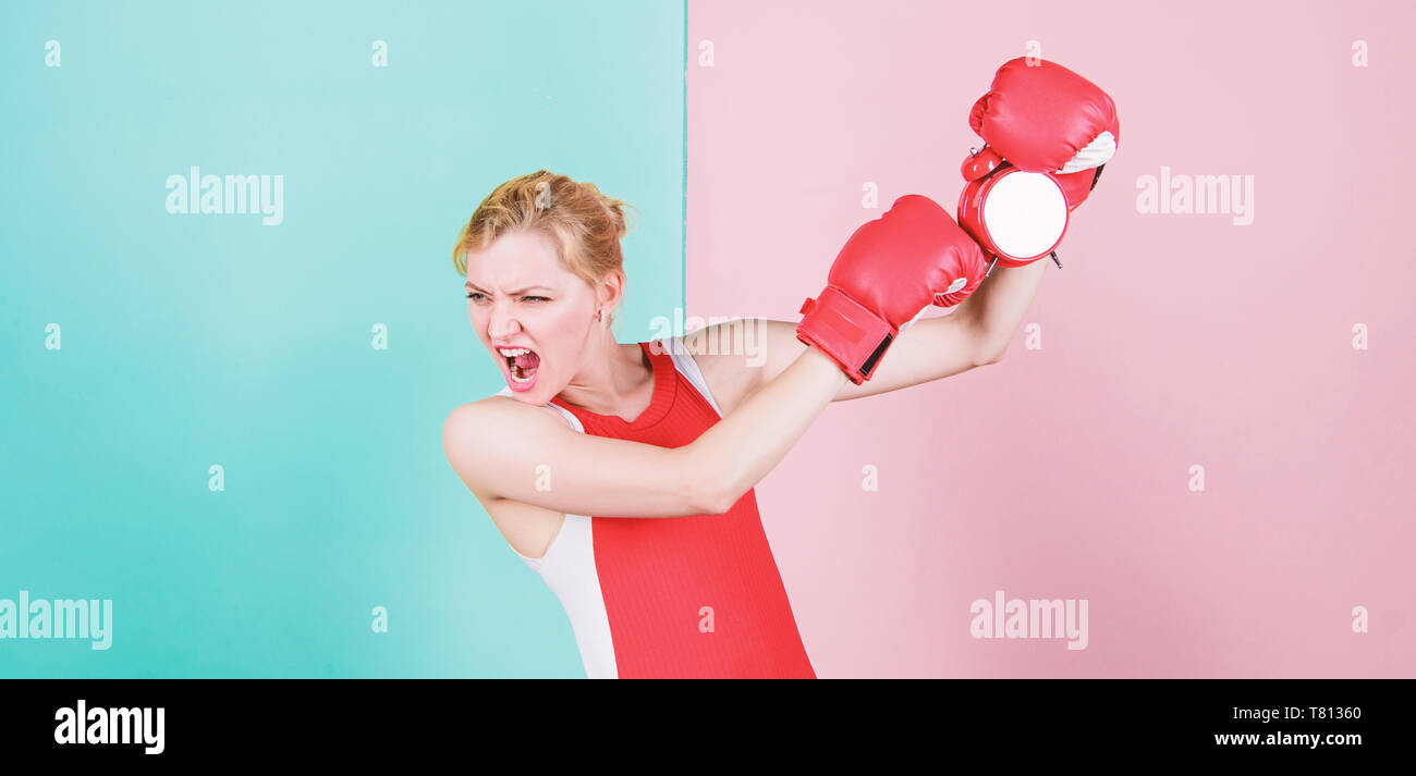 Die Uhr zeigt die falsche Zeit an. Sportlerin stanzen eine Uhr. Emotionale Frau mit Uhr in Boxhandschuhen. Cute Boxer mit wütenden Blick Kampf mit Wecker. Seine Zeit für das Boxtraining. Stockfoto