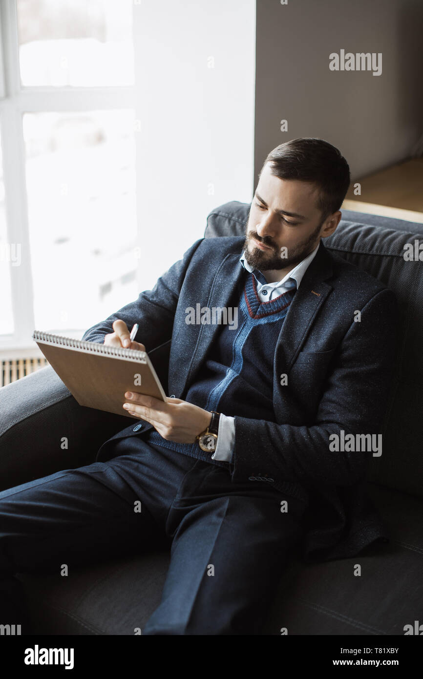 Selbstbewusst Konzentriert Gut Aussehende Bartige Geschaftsmann In Einem Trendigen Anzug Schreibt Wichtige Ideen In Einem Notebook Sitzen Auf Einem Sofa Im Buro Sorbedly Denken Seriose Mann Im Geschaft Tragt Arbeit Stockfotografie