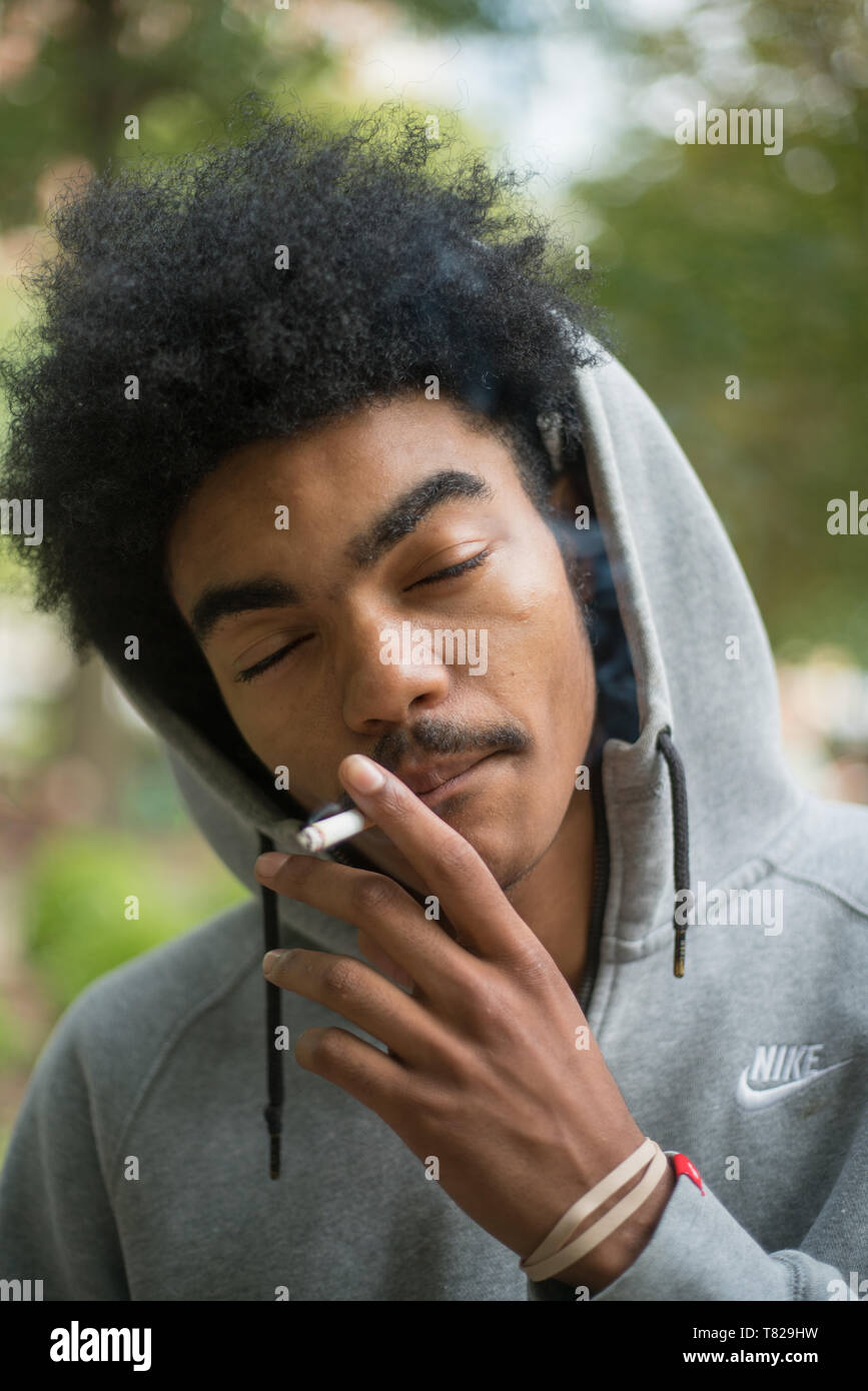 Street Portrait in Philadelphia, Pennsylvania, einer jungen afrikanischen amerikanischen Mann in einem Hoodie Rauchen einer Zigarette außerhalb Stockfoto