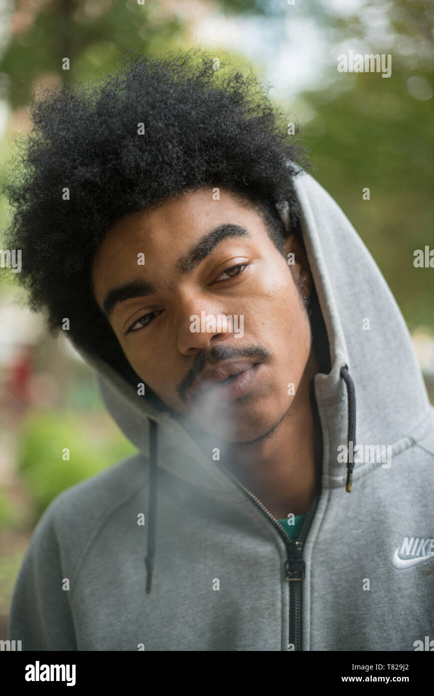 Street Portrait in Philadelphia, Pennsylvania, einer jungen afrikanischen amerikanischen Mann in einem Hoodie Rauchen einer Zigarette außerhalb Stockfoto