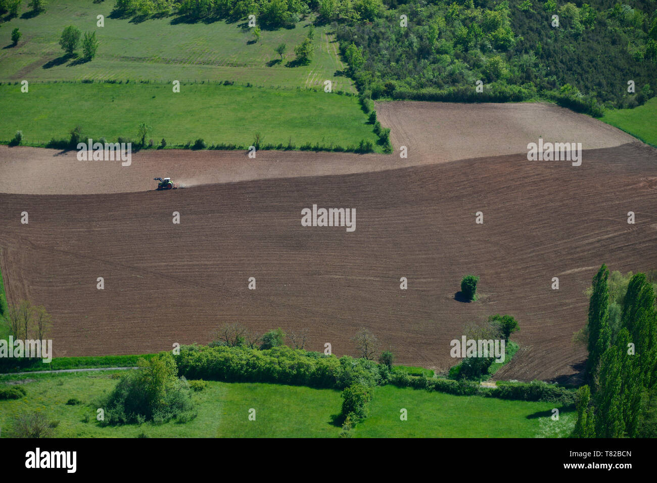 Ein langer Schuß eines Traktors, mit einer Spur von Staub, Pflügen eine zweifarbige braune Feld in Süd frankreich. Stockfoto