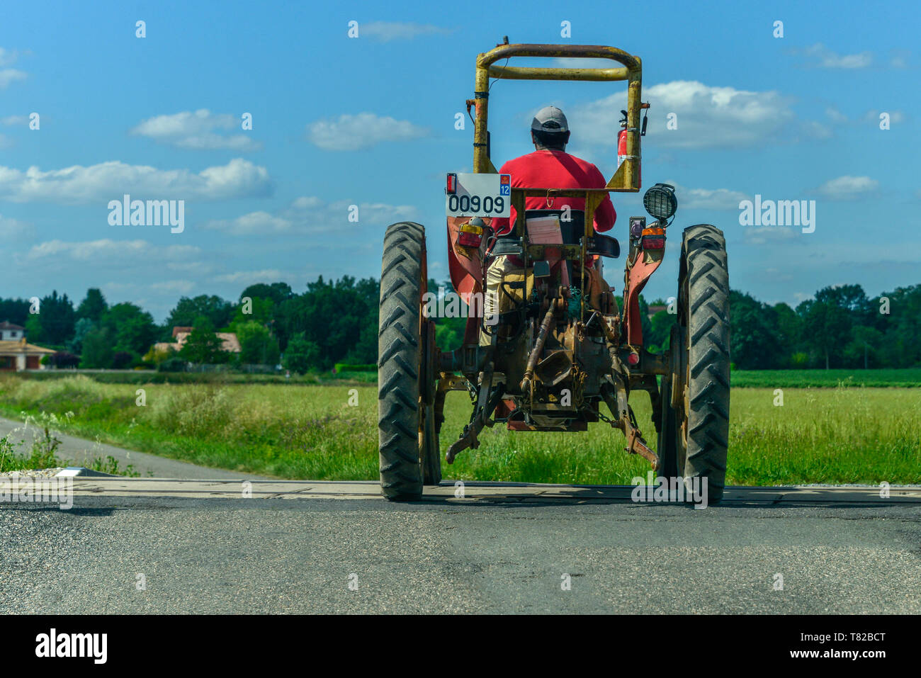 Eine Rückansicht eines französischen Bauern in einem Traktor mit dünnen Reifen, Überqueren einer Bahnstrecke. In der Nähe von Gaillac, Royal, Frankreich. Stockfoto