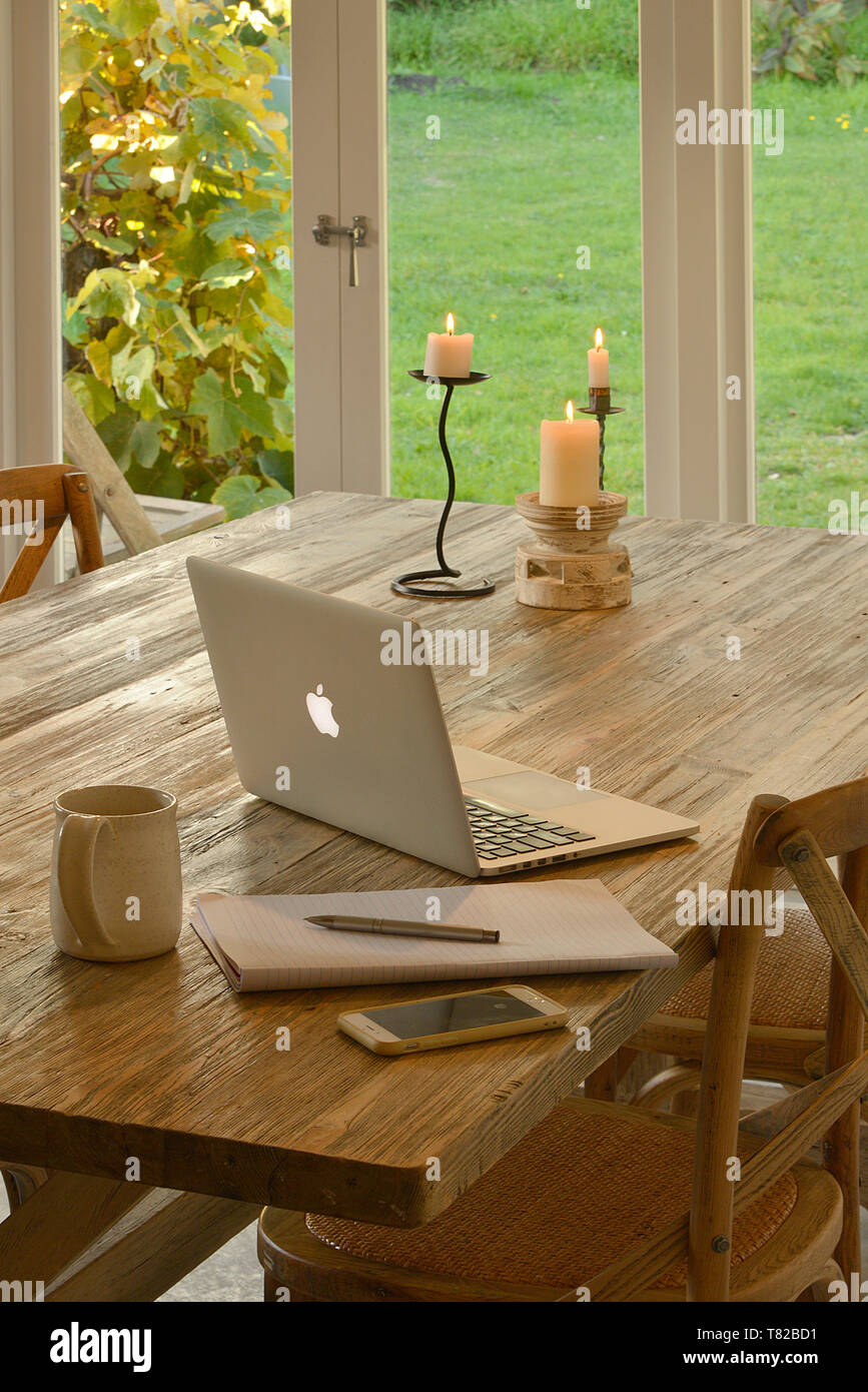 Arbeiten von zu Hause aus. Ein rustikaler Holztisch mit einem Laptop, Kerzen, einen schreibblock füllen Sie die Szene. Eine Ovation Gitarre lehnt sich gegen die Wand. Stockfoto