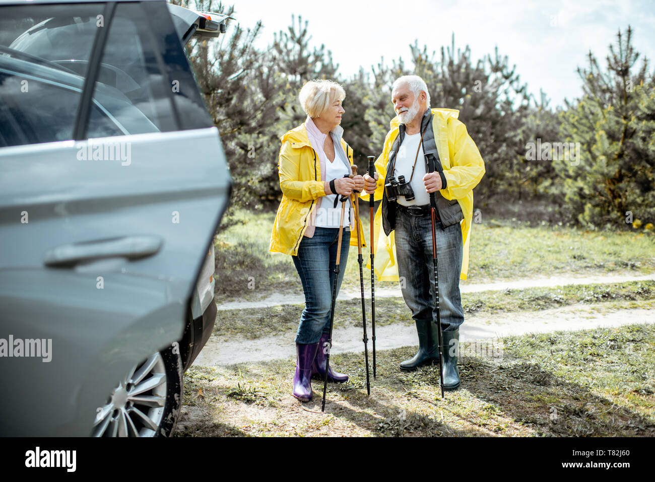 Senior Paar in gelbe Regenmäntel nahe dem Auto in den Wald, um ihren Ruhestand genießen. Stockfoto