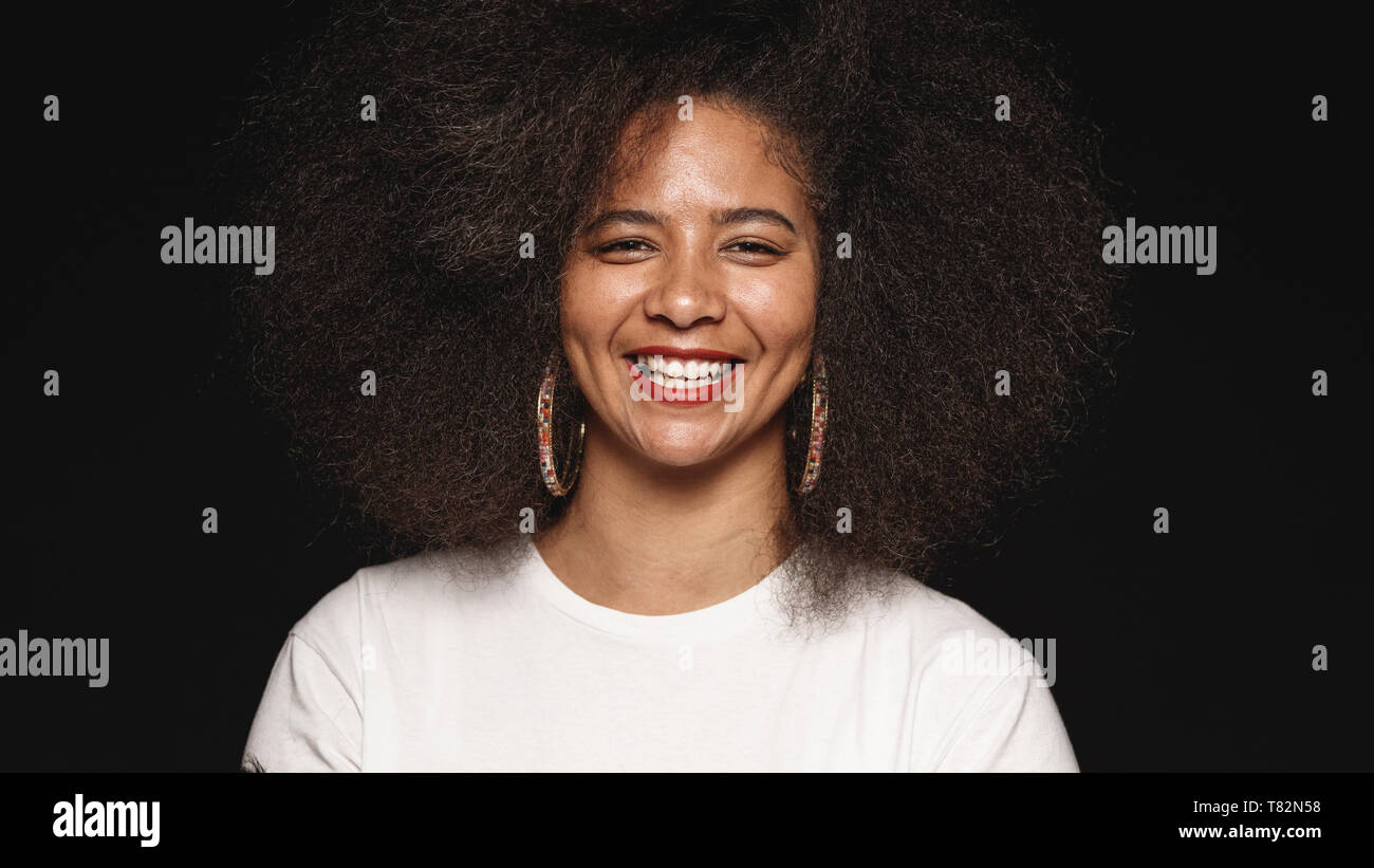 Happy african american Female in Afro Frisur auf schwarzem Hintergrund isoliert. Der lächelnde Frau mit Kamera schaut. Stockfoto