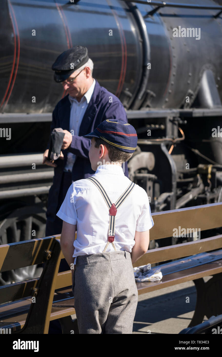 Severn Valley Railway - Kriegszeit der vierziger Jahre Großbritanniens. Rückansicht Nahaufnahme, Schuljunge in Vintage-Schulkappe und Hosenbandspangen, die Dampfzüge auf dem Bahnsteig beobachten. Stockfoto